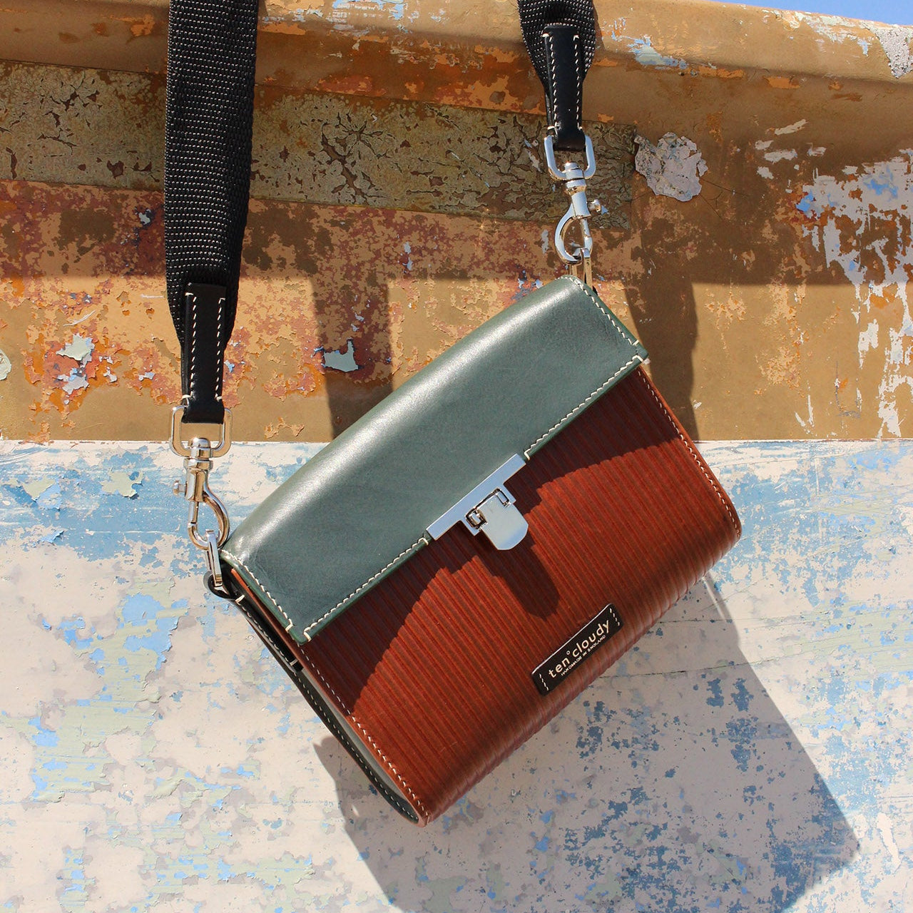 Two-tone handbag with a strap on a textured surface with blue sky background