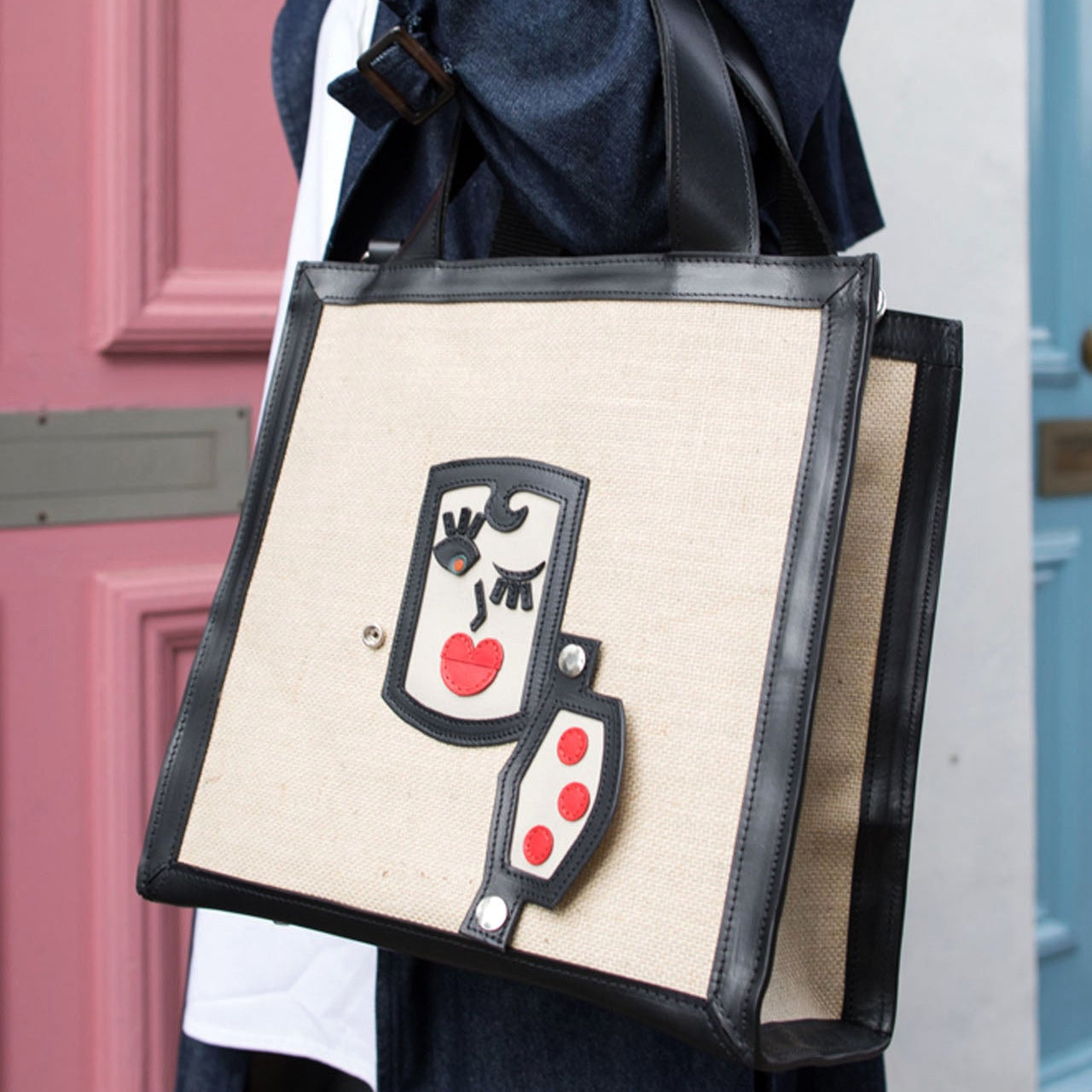 Person holding a tote bag with a unique design in front of a pink door.
